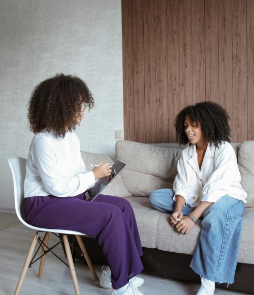 Two women in conversation during a therapy session, featuring informal seating and relaxed attire.