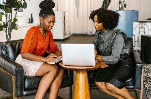 Two African American women collaborating in a cozy office space, focused on a laptop.