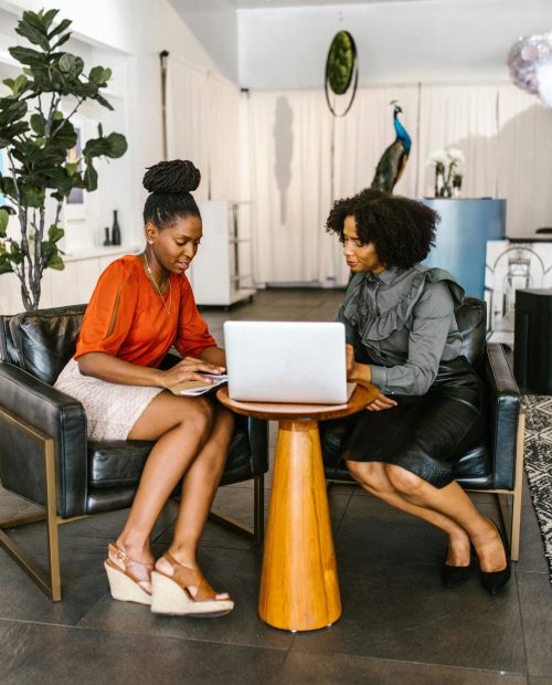 Two African American women collaborating in a cozy office space, focused on a laptop.