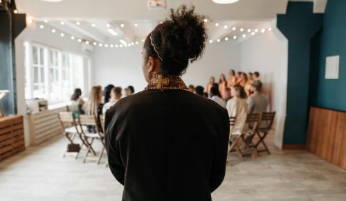 A pastor stands at the altar in a modern church setup with parishioners and a choir in the background.